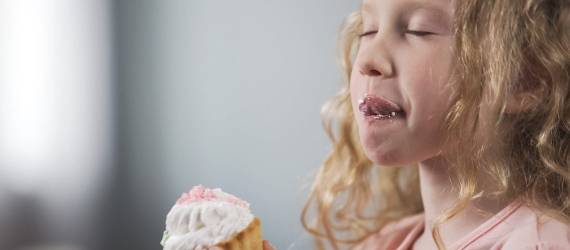Adorable little girl eating cake with appetite enjoying perfect taste of dessert